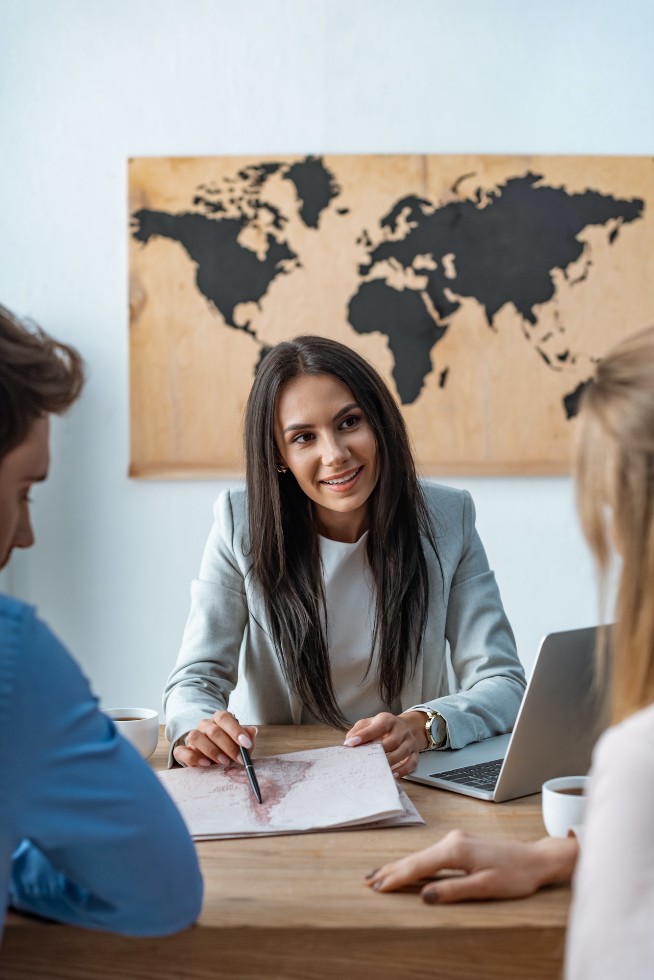 smiling travel agent pointing with pen at map near couple of tourists